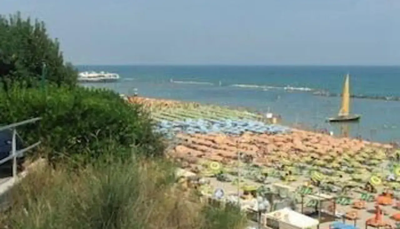 Spiaggia affollata con ombrelloni colorati e un veliero al largo, vista panoramica dal **hotel Plaza Gabicce Mare**.