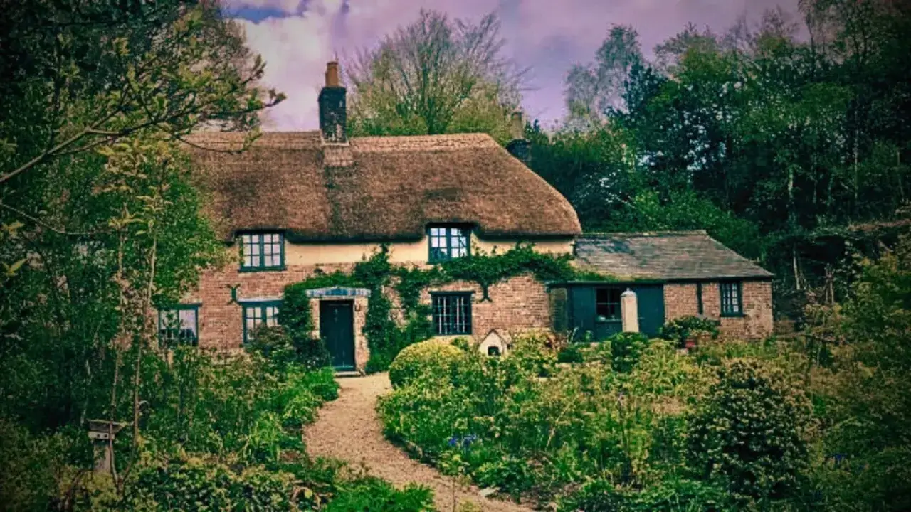 Urokliwy domek z krytym strzechą dachem, otoczony bujną zielenią. Idealne miejsce do czytania **Thomas Hardy książki**.