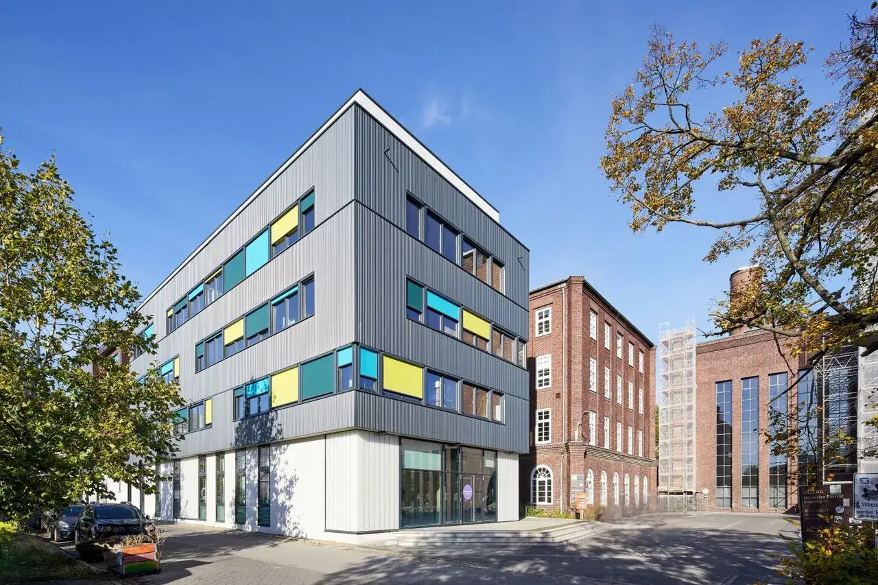 Modernes Geb&auml;ude mit bunten Fensterl&auml;den, neben einem Backsteinbau. Ein Ort, der das 