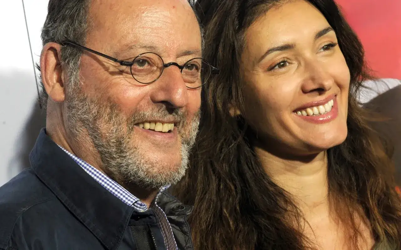 Jean Reno z żoną, uśmiechnięci, patrzą w bok.