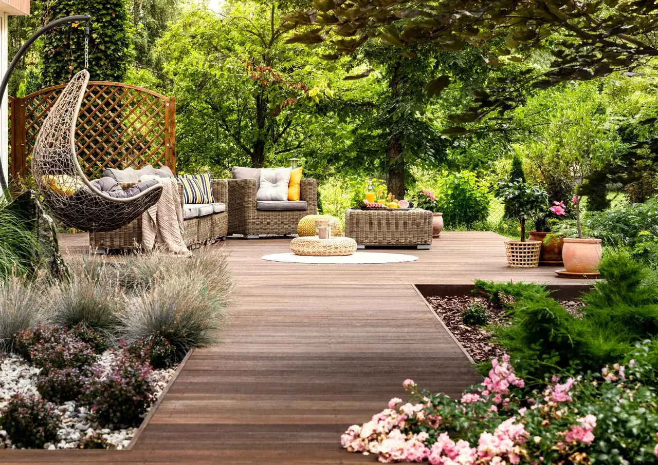 Un idílico **jardín de verano** con muebles de mimbre, una mecedora colgante y exuberante vegetación. Perfecto para relajarse.