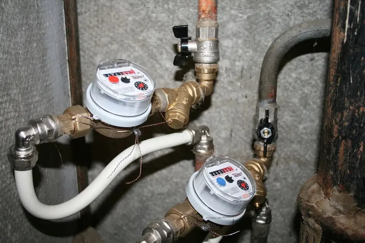Deux compteurs d'eau sont install&eacute;s sur des tuyaux en laiton. L'ouverture compteur eau locataire est visible sur les deux appareils.