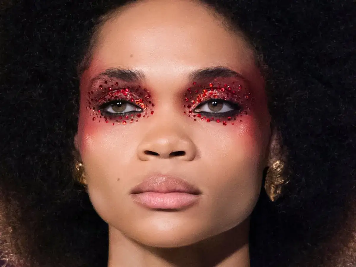 En kvinna med dramatisk ögonmakeup i rött glitter och guldörhängen. En doft av amber kan anas i hennes utstrålning.