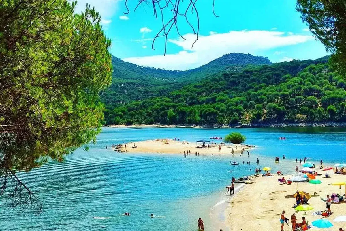 Gente disfrutando del sol y el agua en la playa de Arija, rodeada de exuberante vegetación y montañas.