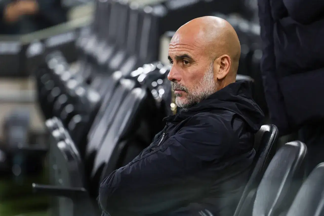 Pep Guardiola, znany z tego, że prowadzone drużyny osiągają sukcesy, siedzi na ławce rezerwowych, zamyślony.
