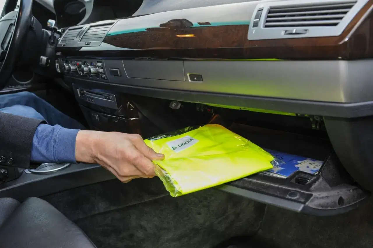 Hand nimmt eine gelbe Warnweste aus dem Handschuhfach. So viele Warnwesten im Auto sind wichtig f&uuml;r die Sicherheit.