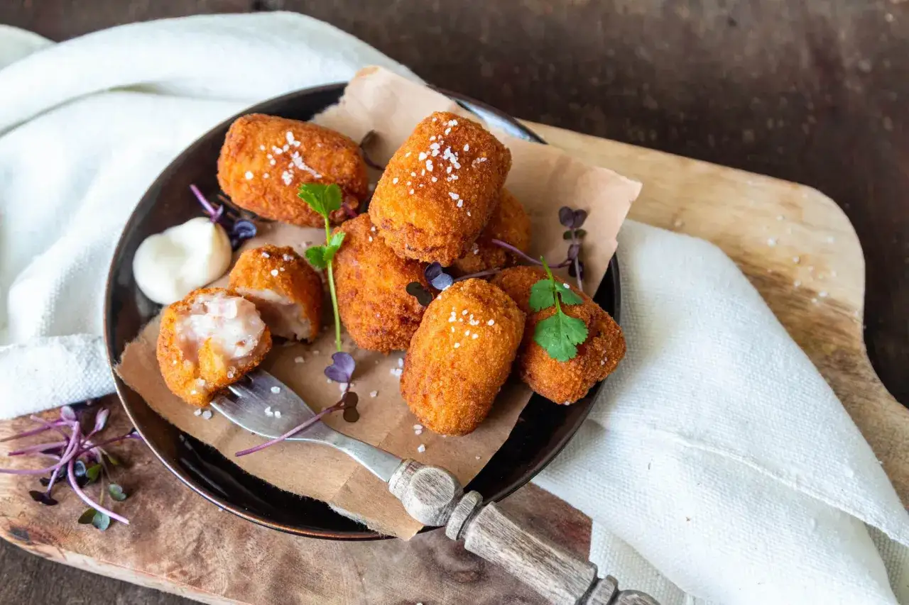 Assiette de croquetas espagnoles dor&eacute;es et croustillantes, garnies de sel et de persil, avec une touche de mayonnaise.