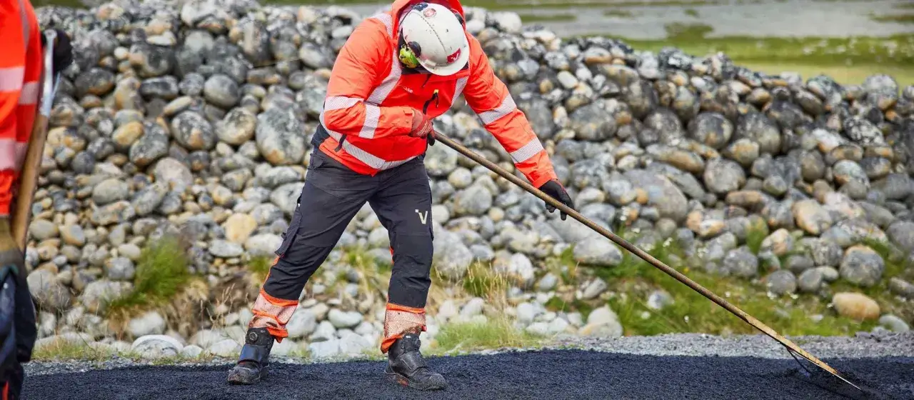 Arbetare asfalterar uppfart med en r&auml;fsa. En stenmur syns i bakgrunden.