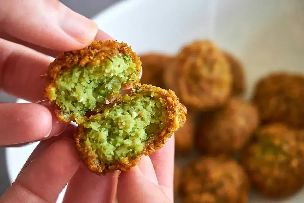 En hand håller en delad falafelboll med grön, fluffig insida. Perfekt för ett enkelt falafel recept!