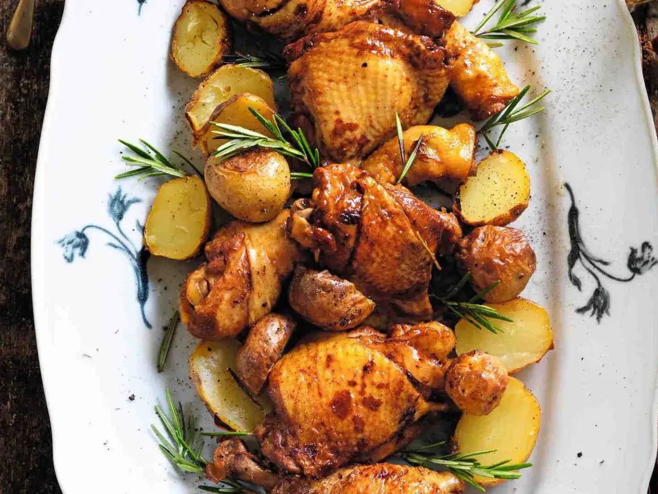 Pollo alla birra succulento e patate arrosto su un piatto bianco decorato, guarnito con rosmarino fresco.