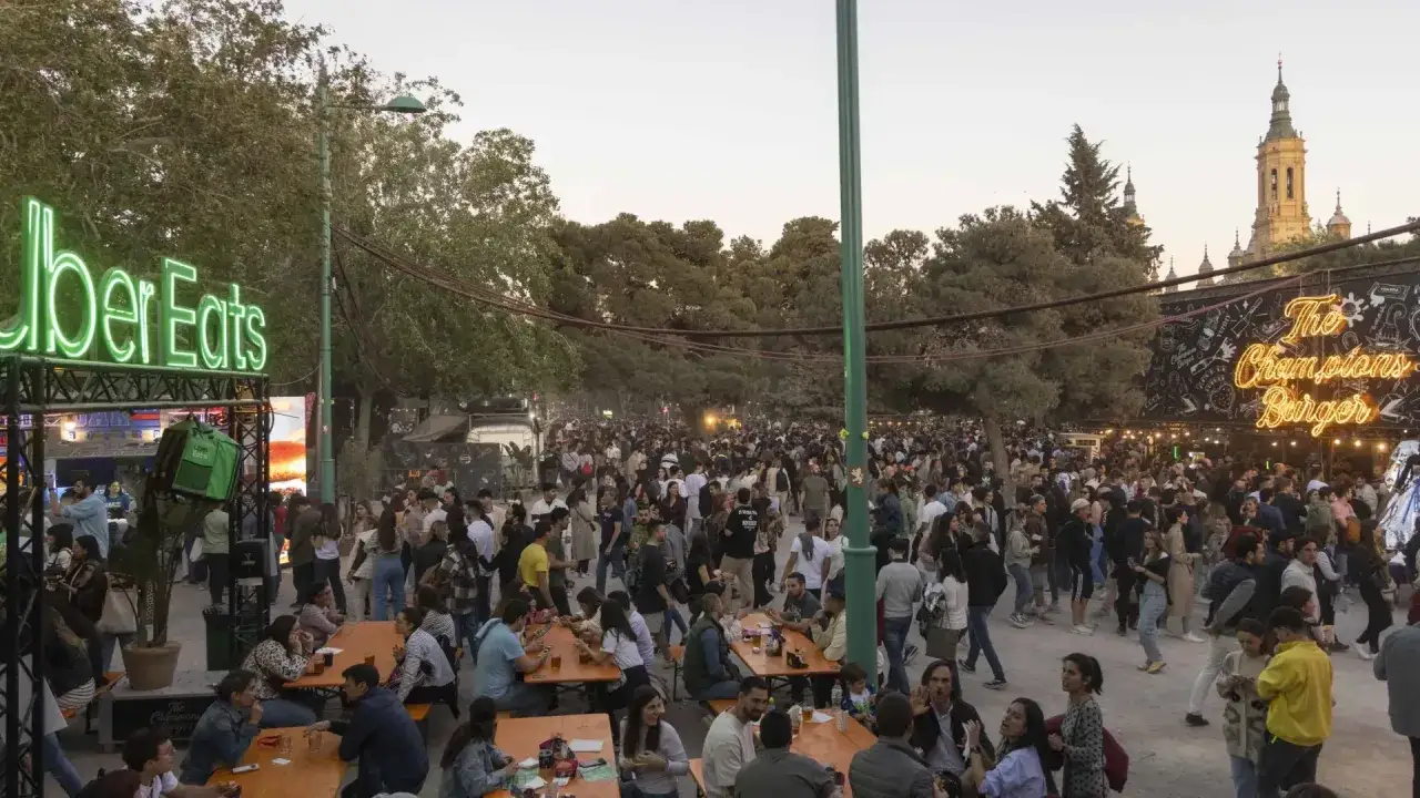 Multitud disfrutando en un evento al aire libre en Zaragoza, con un letrero de neón de