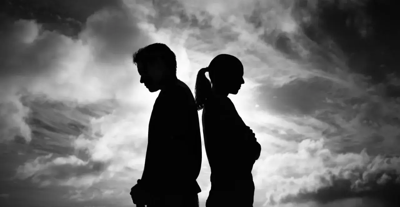 Silhouetten eines Paares, R&uuml;cken an R&uuml;cken, vor dramatischem Himmel. Ihre K&ouml;rperhaltung dr&uuml;ckt Entfremdung aus, ein Gef&uuml;hl von Angst und verlorener Liebe.