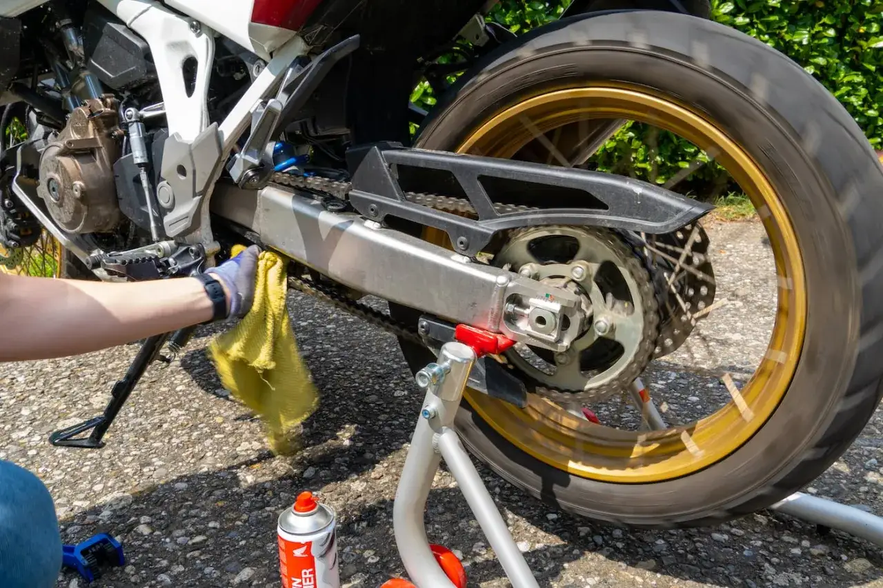 Mano con guanto pulisce la catena della moto, un po' di ruggine catena moto è visibile.