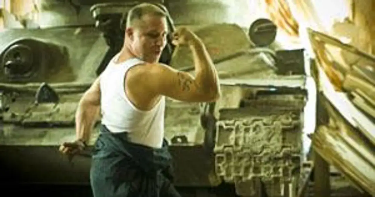 Mięśniak w podkoszulku napina biceps obok czołgu, gotowy do operacji Dunaj.