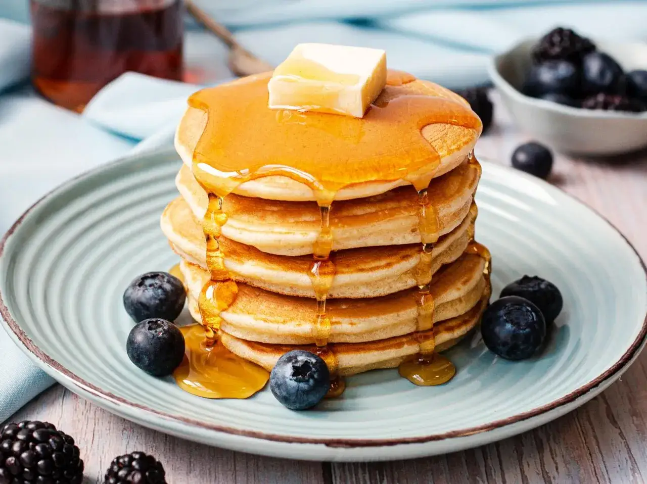 Ein Stapel Mini-Pfannkuchen mit Honig und Butter, garniert mit Blaubeeren. Perfekt f&uuml;r ein schnelles Mini-Pancakes-Rezept!