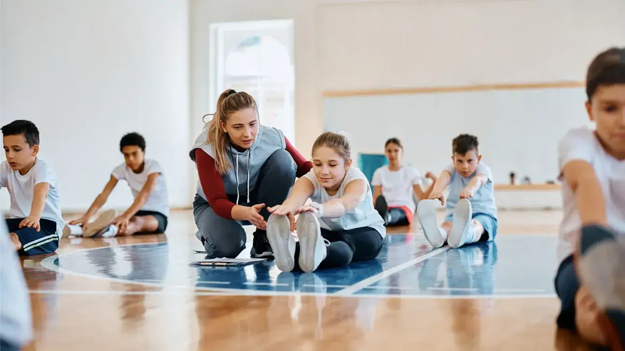Nauczycielka pomaga dzieciom w ćwiczeniach rozciągających, realizując edukacja zdrowotna program nauczania.