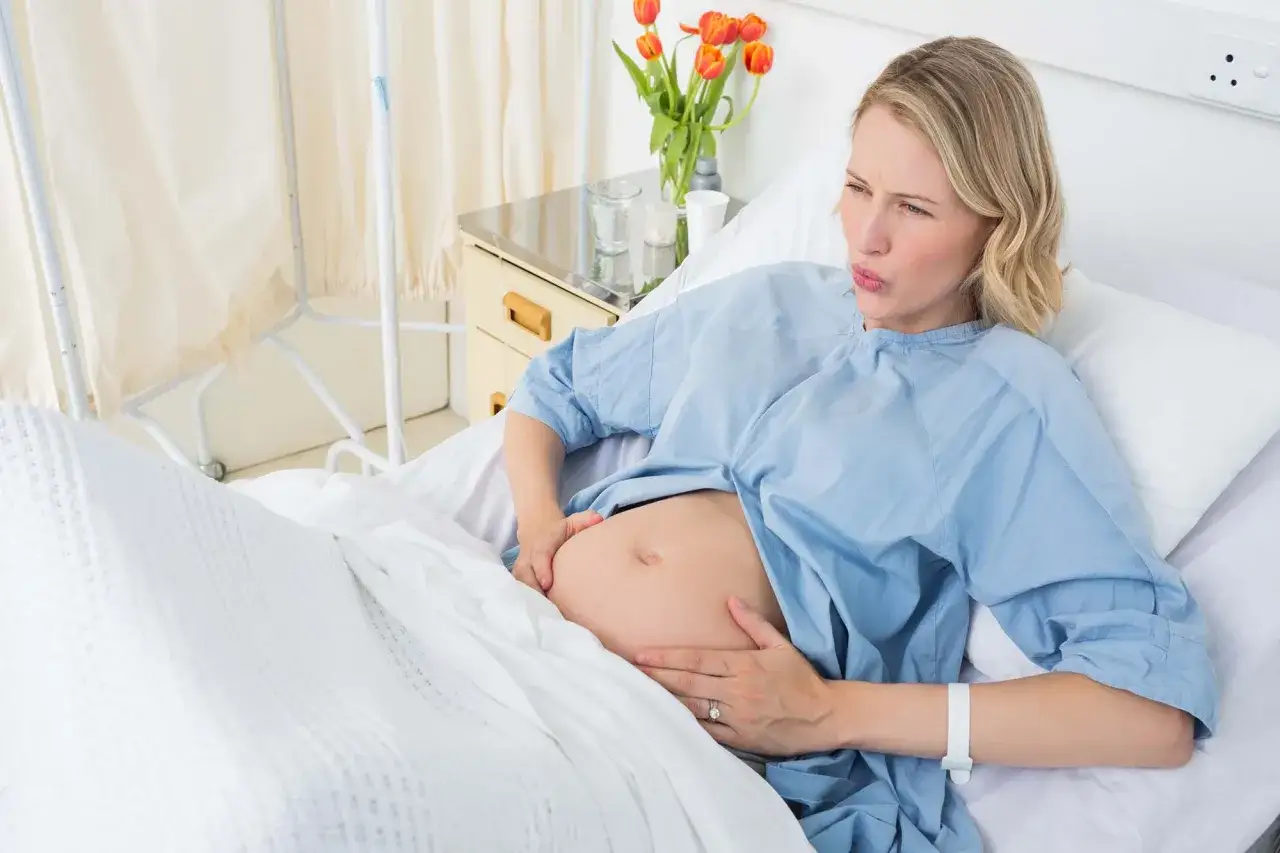 Gravid kvinna i sjukhuss&auml;ng, h&aring;ller magen. Hon ser ut att ha ont, kanske vattnet har g&aring;tt.