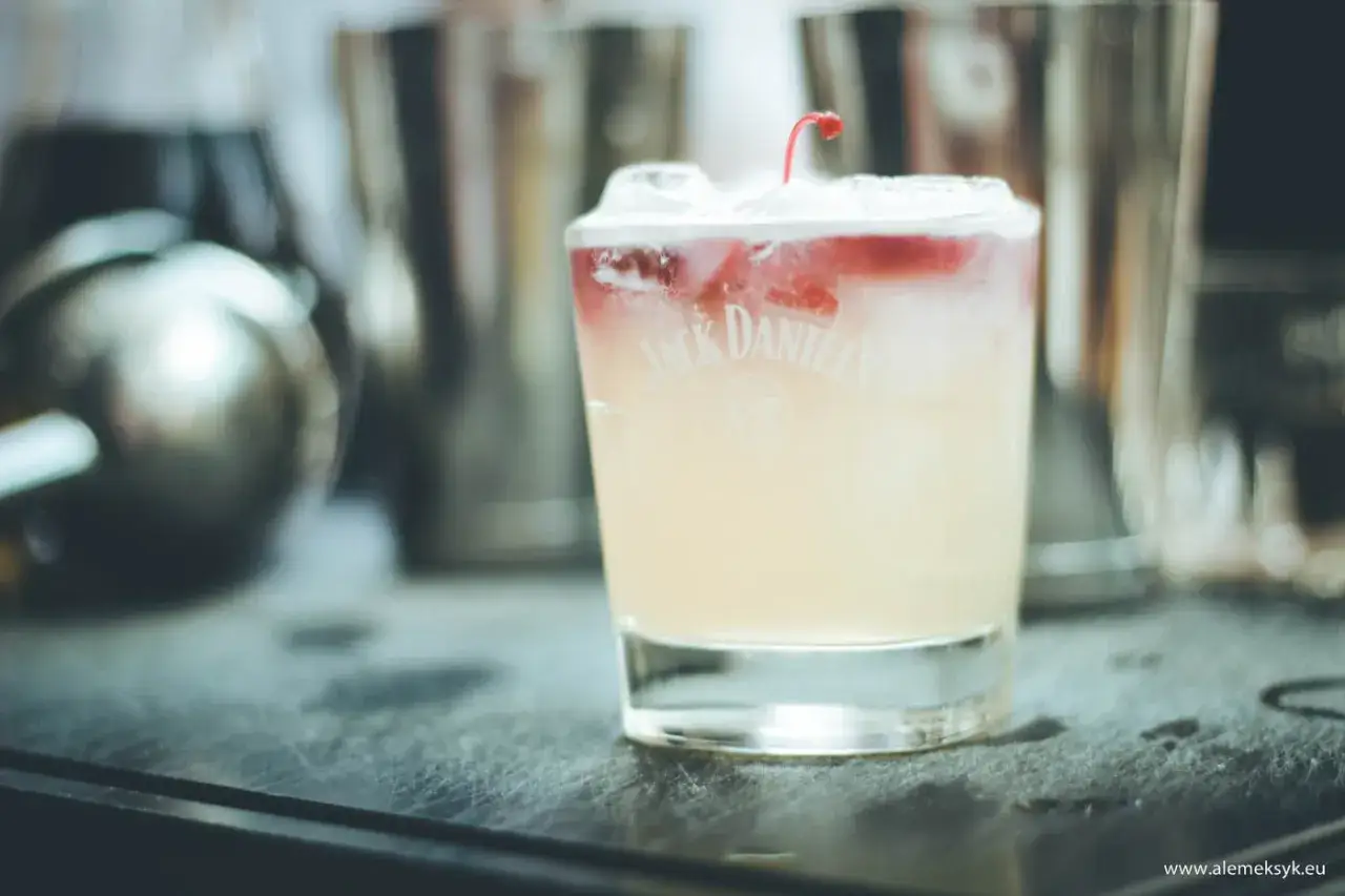 Orzeźwiający New York Sour z wiśnią na wierzchu, przygotowany w szklance z logo Jack Daniel's, na tle barmańskich shakerów.