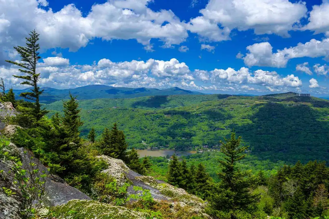 Scenic mountain vista with a lake, perfect for day trips from Richmond, VA. Lush green forests under a bright blue, cloudy sky.