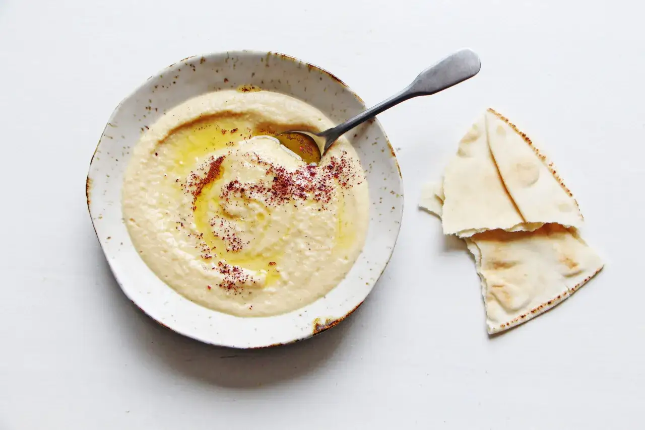 Houmous maison crémeux dans un bol, arrosé d'huile d'olive et saupoudré d'épices, avec du pain pita à côté. Parfait pour une recette facile.