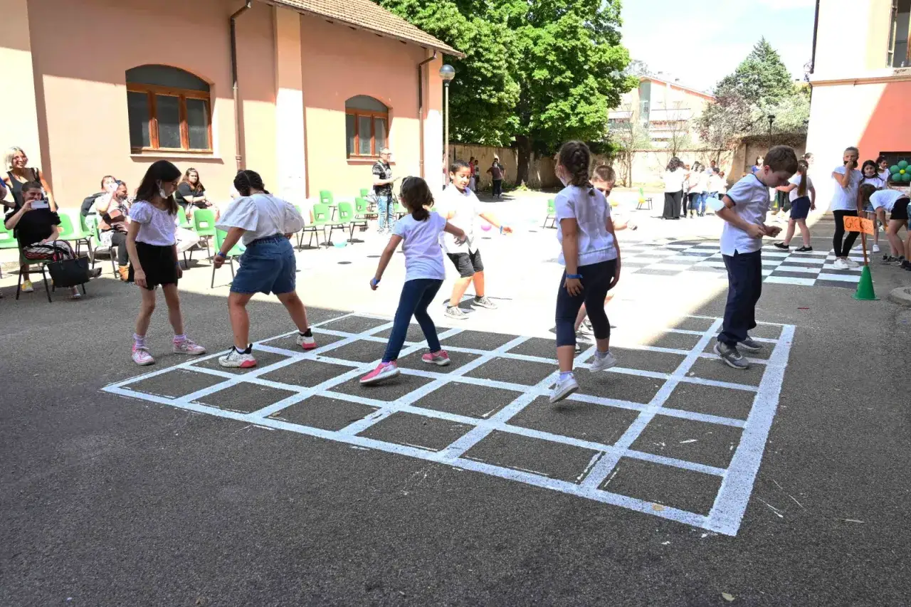 Bambini giocano alla campana, uno dei giochi popolari per bambini, in un cortile soleggiato.