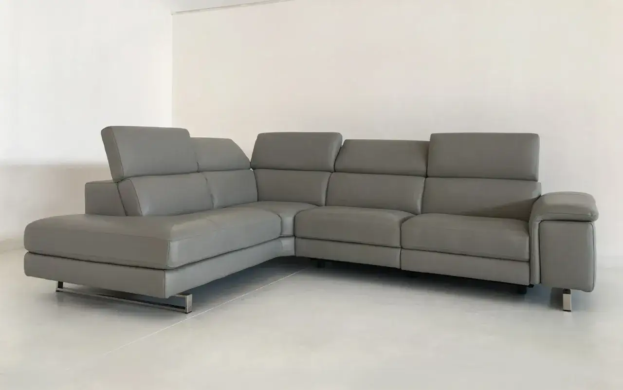 Divano angolare grigio in **full grain leather**, con poggiatesta regolabili e piedini in metallo.