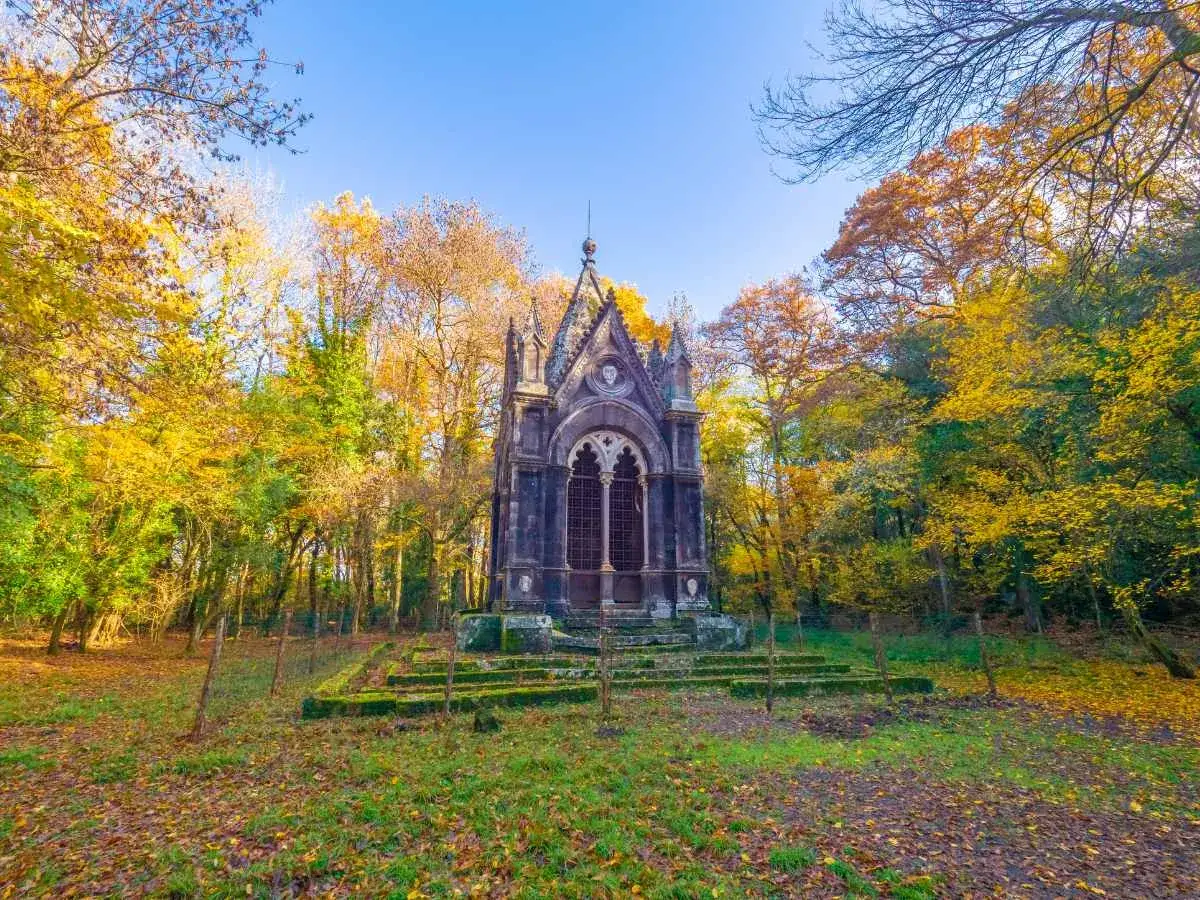 Un'antica cappella gotica immersa nel bosco delle fate di Acquasparta, con alberi dalle foglie dorate e un cielo azzurro.