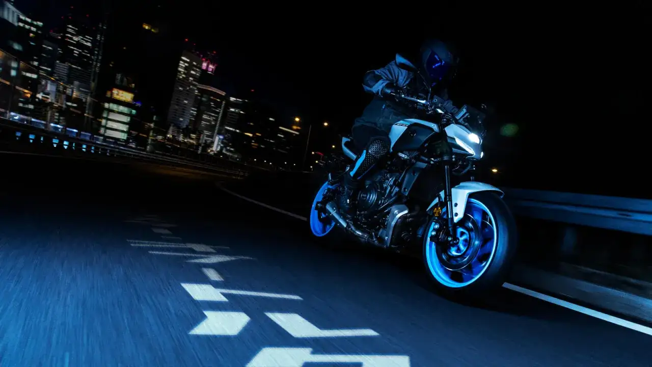 Una Yamaha scarenata sfreccia di notte in citt&agrave;, con luci al neon che illuminano la strada e la moto.