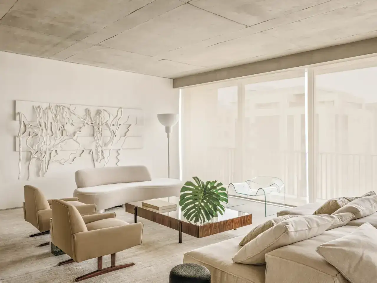 Salón moderno con sofá curvo y sillones beige, arte abstracto en la **ral 9010 pared**, mesa de centro de madera y cristal, y grandes ventanales.