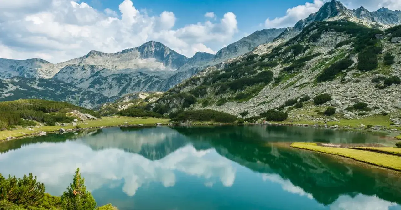 Górskie jezioro odbija chmury i skaliste szczyty. Krajobraz przypomina dzikie parki narodowe w Rosji, pełne surowego piękna.