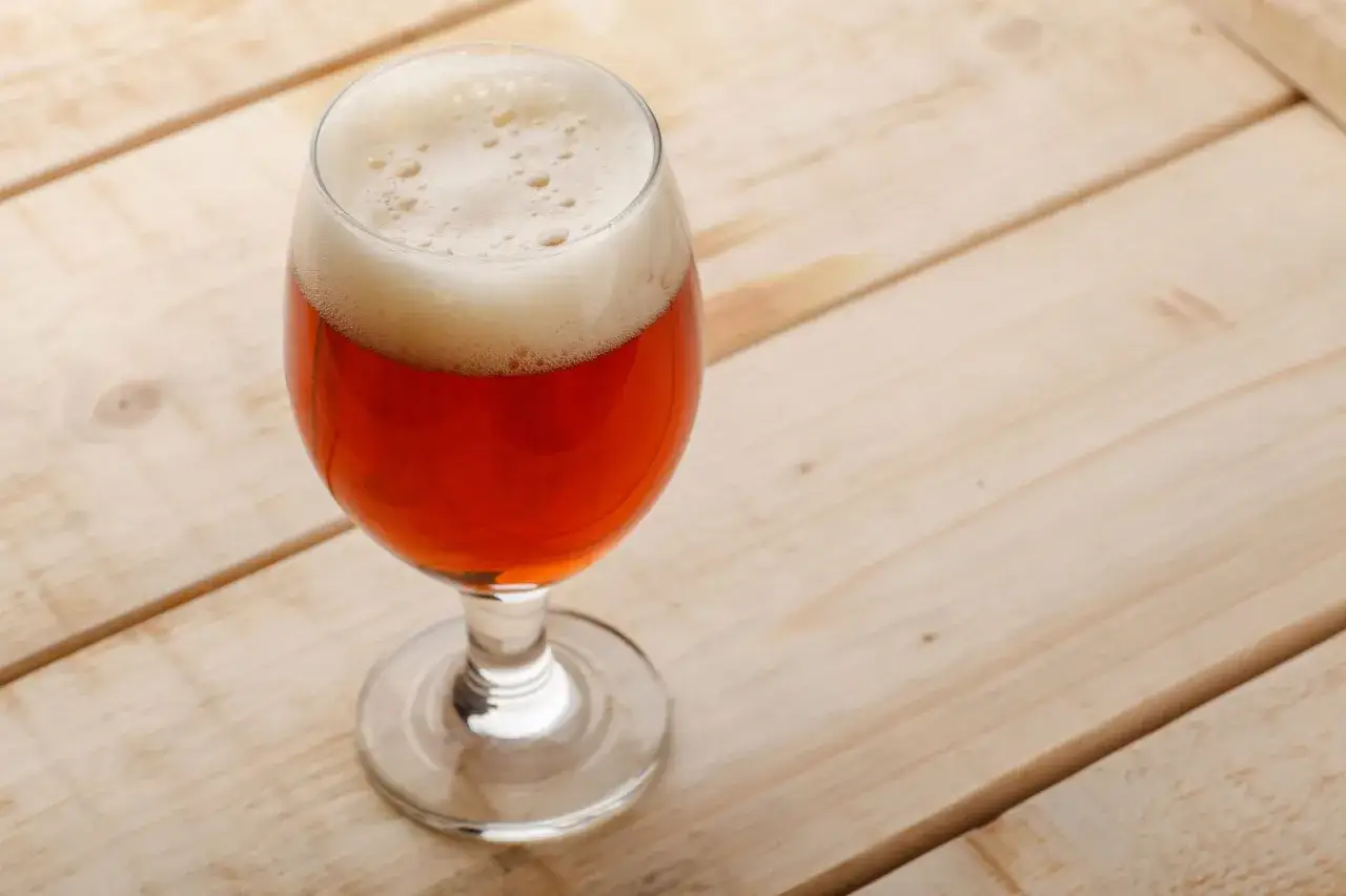 Verre de Belgian Pale Ale ambr&eacute;e, sur fond de planches de bois claires.