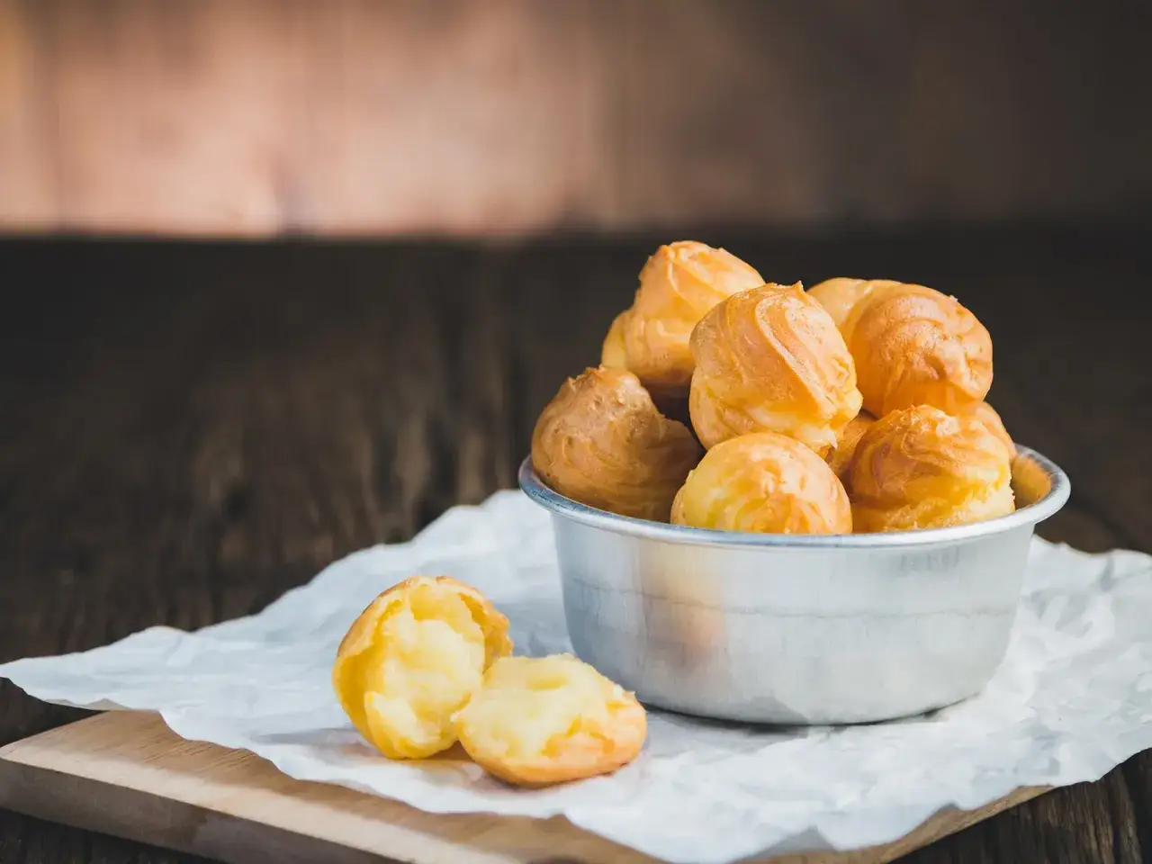 Sch&uuml;ssel voller goldbrauner Windbeutel, die zum original profiteroles rezept geh&ouml;ren. Einer ist aufgeschnitten und zeigt die cremige F&uuml;llung.