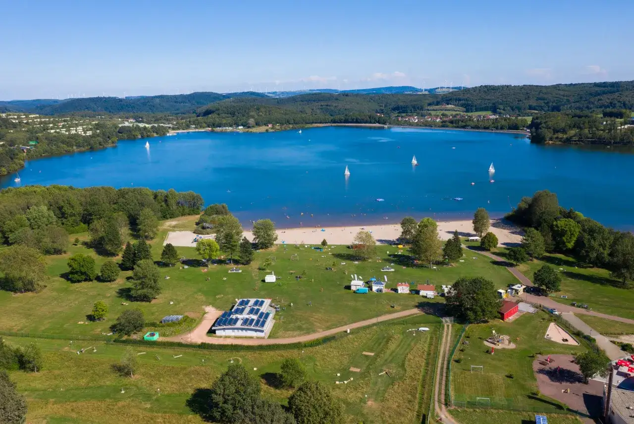 Sonnige Aussicht auf das Bostalsee Strandbad mit vielen Badeg&auml;sten, Segelbooten und gr&uuml;nen Liegewiesen.