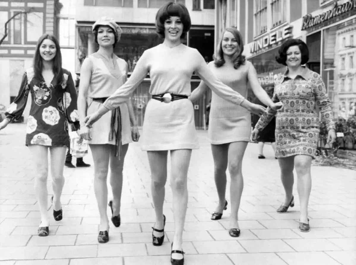 Cinco mujeres con minivestidos y botas de tacón alto, un estilo icónico de Mary Quant, pasean por la calle.