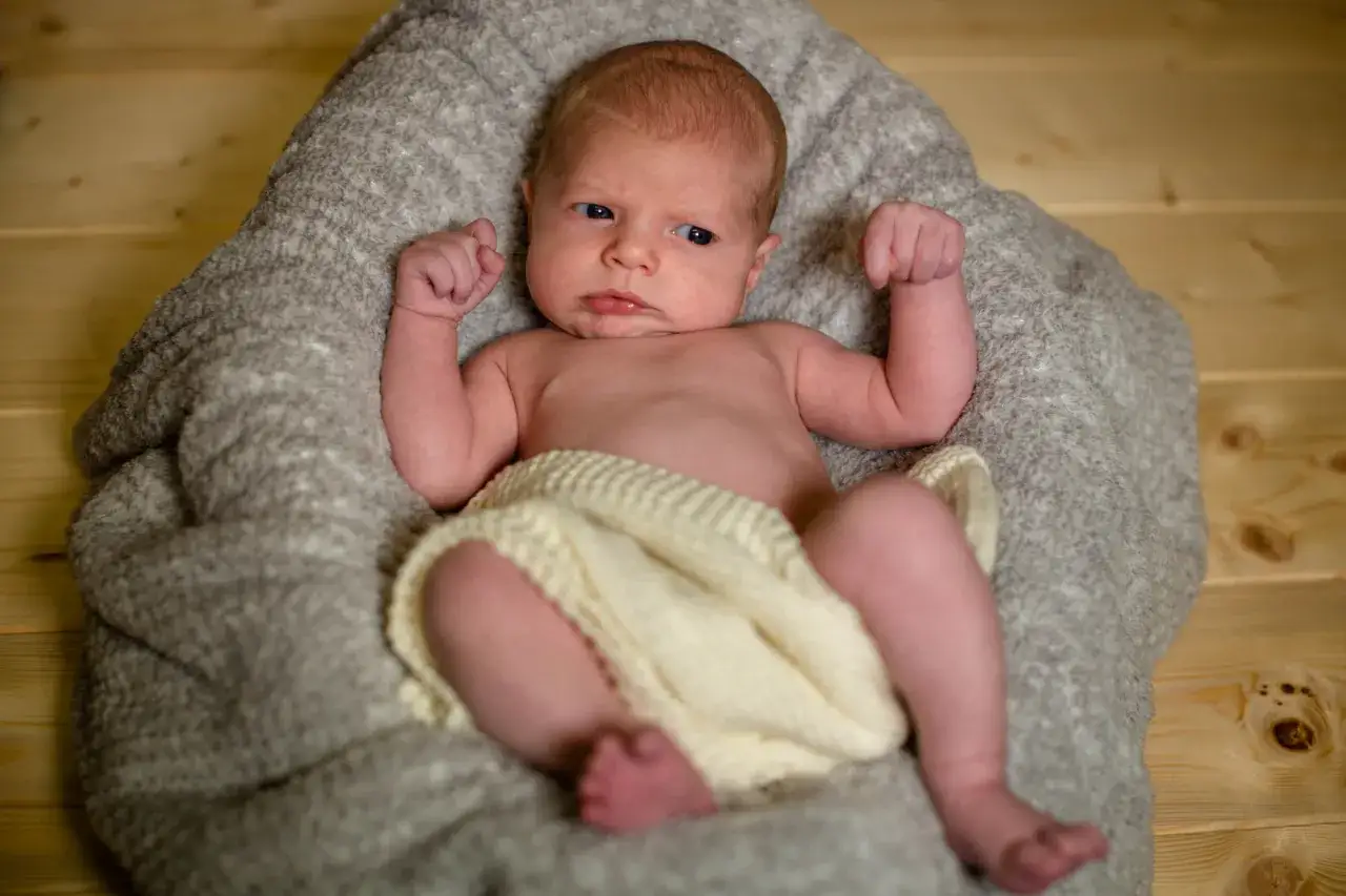 Un neonato con un'espressione curiosa, avvolto in una coperta, pronto per un servizio fotografico flash neonati.