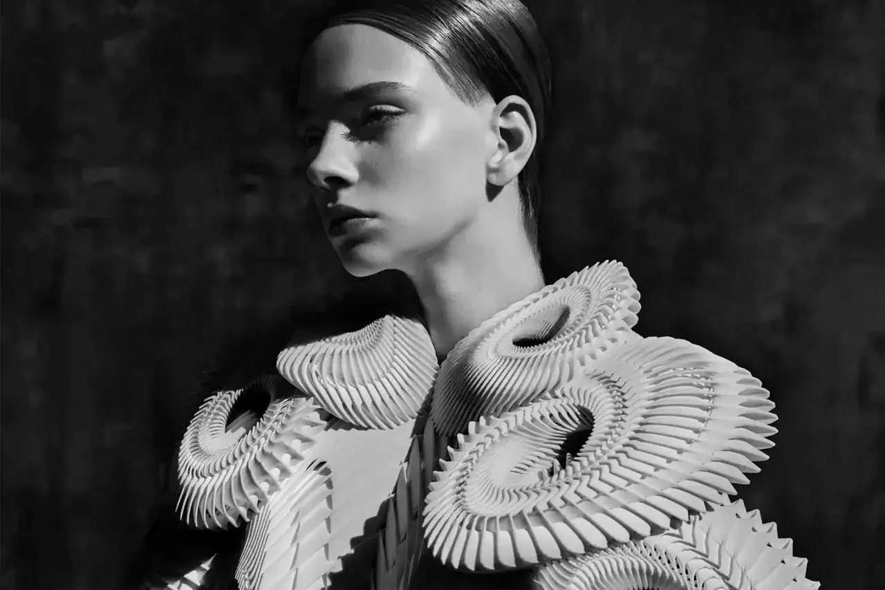 A model showcases intricate, sculptural white garments, embodying futuristic fashion. The detailed textures and avant-garde design create a striking visual.