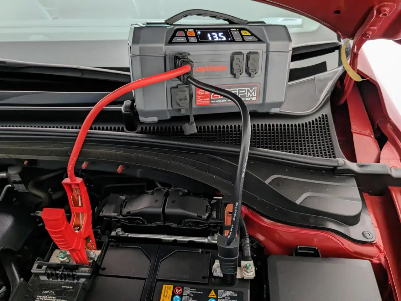 A jump starter is connected to a car battery, showing 13.5V. This answers the question: do jump starters come charged? Yes, they do.