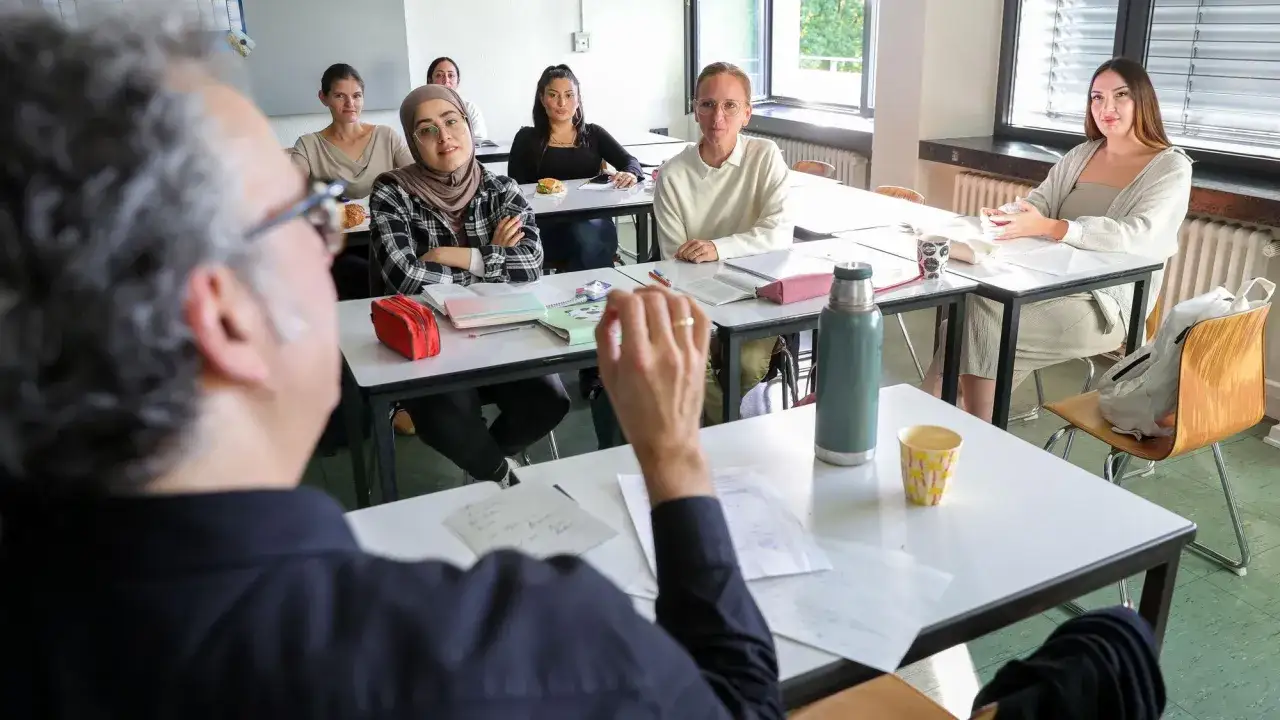 Lehrer erklärt Schülern, wie man sein Abi nachholen kann. Sie sitzen im Klassenzimmer, lernen und hören aufmerksam zu.