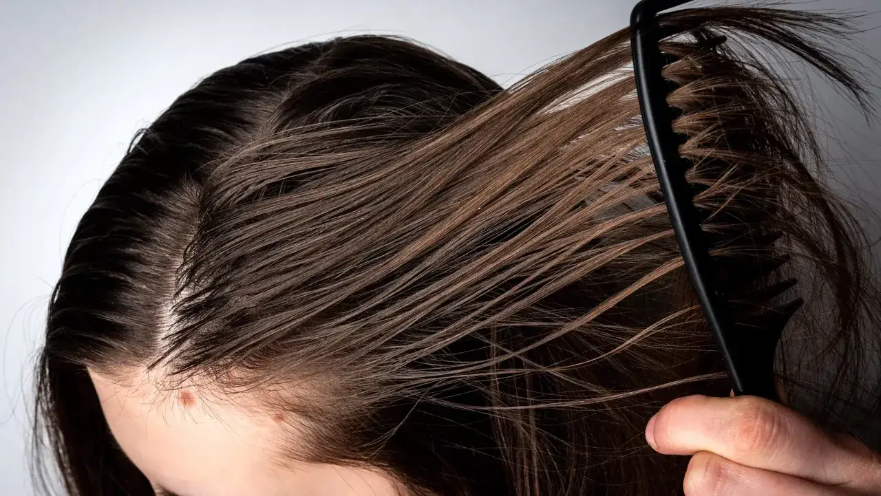 Primer plano de una mujer peinando su pelo graso. Se ve el cuero cabelludo y mechones de cabello casta&ntilde;o.