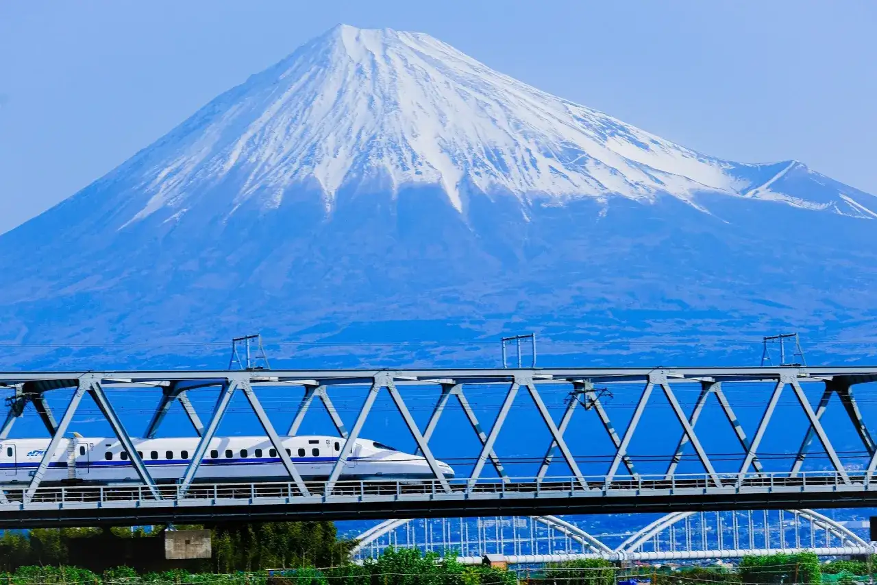 Szybki pociąg Shinkansen przejeżdża przez most z widokiem na ośnieżony szczyt góry Fudżi. Idealna Japonia wycieczka!