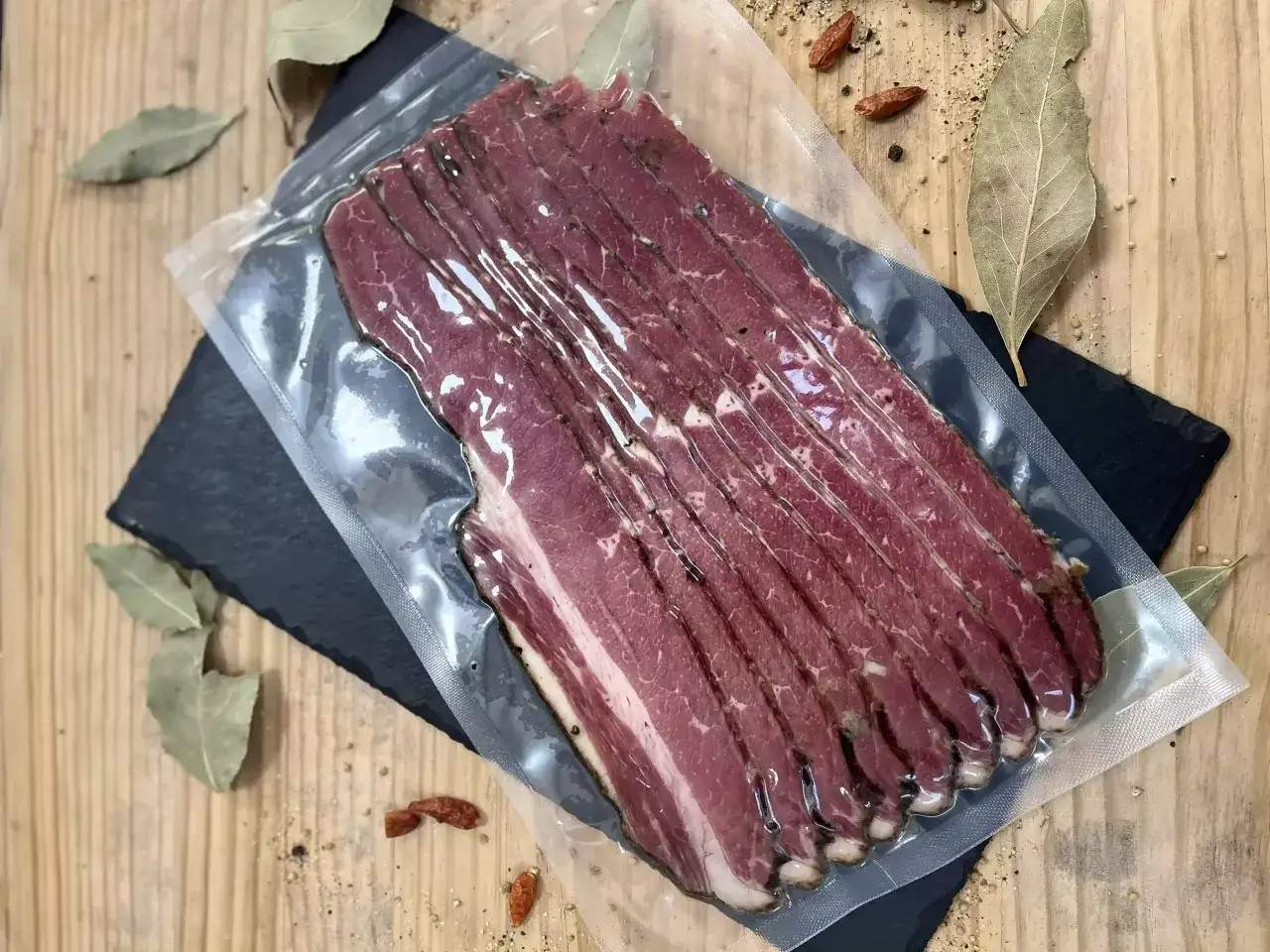 Lonchas de pastrami que es carne curada y ahumada, listas para disfrutar. Se aprecian especias y hojas de laurel alrededor.