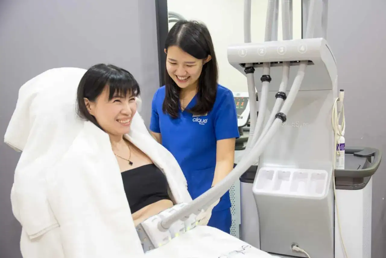 Une femme souriante reçoit un soin minceur dans un institut, assistée par une esthéticienne.