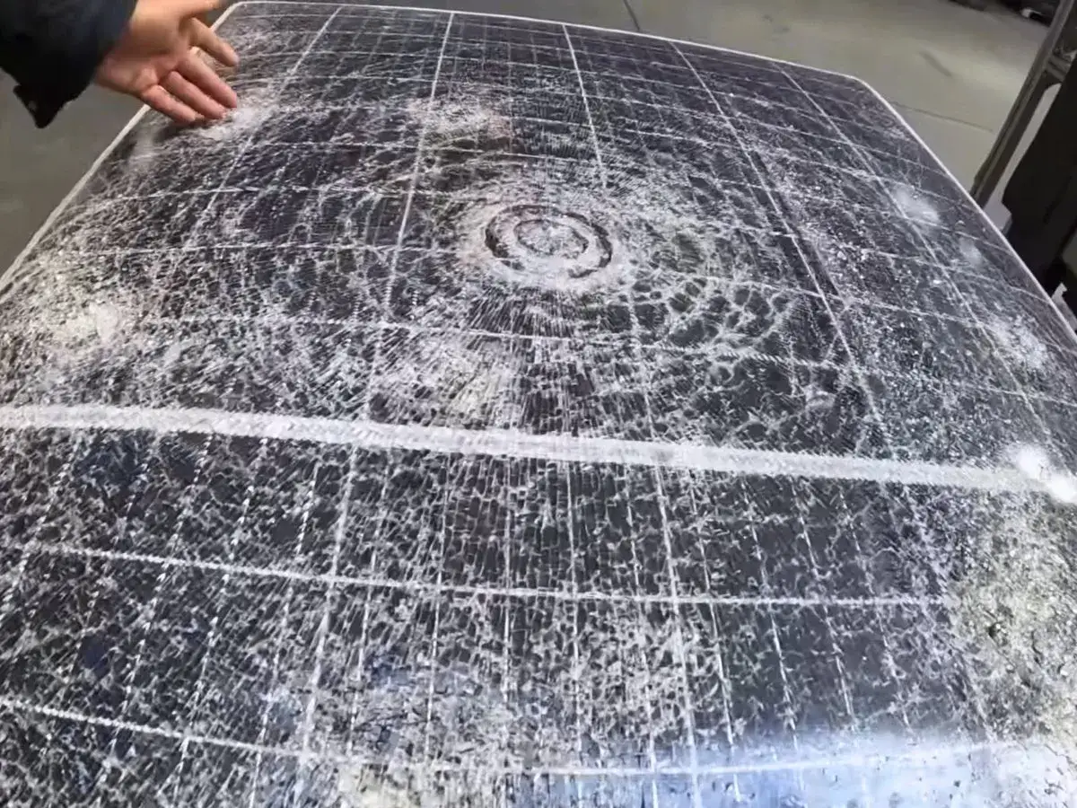 Panneau solaire endommagé par la grêle, montrant de multiples impacts et fissures sur sa surface.