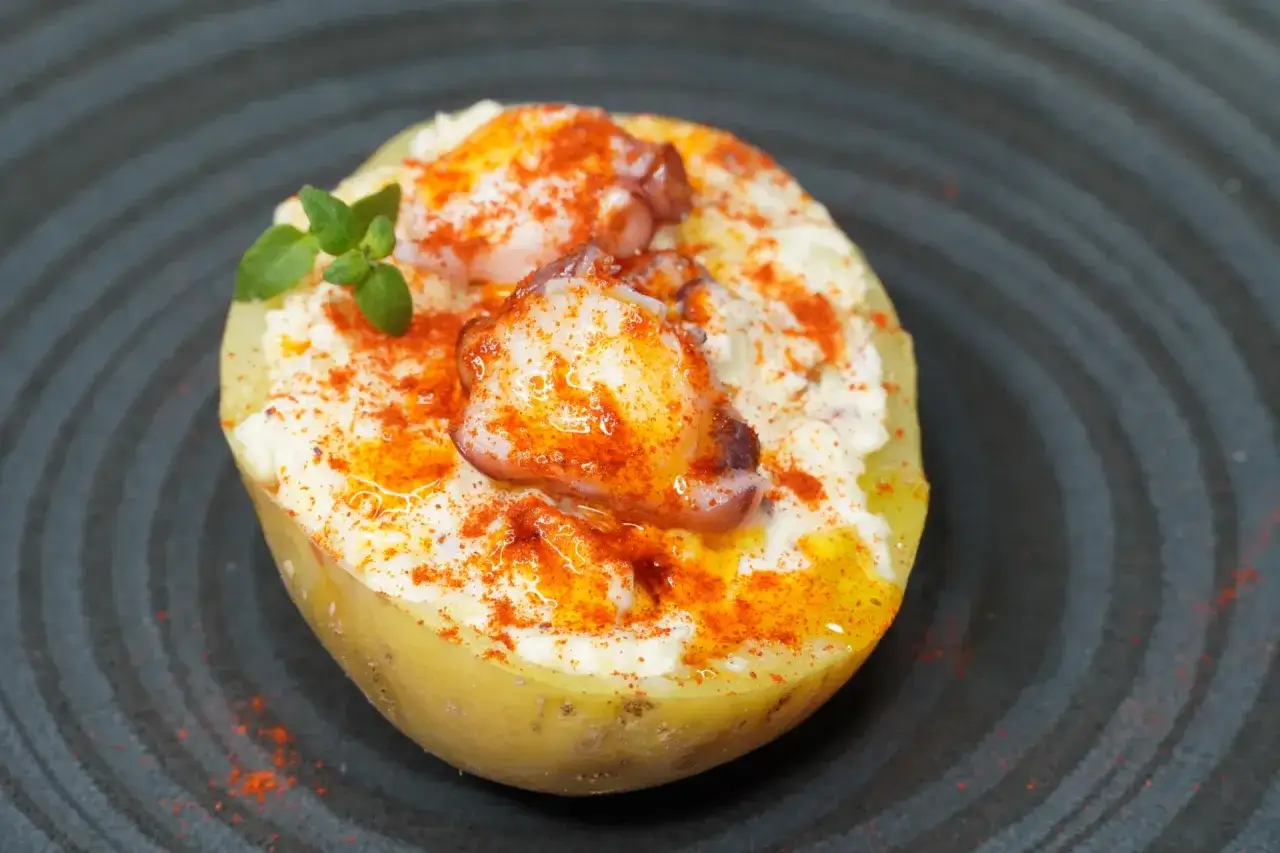 Patata rellena con ensaladilla de pulpo, cremosa y espolvoreada con piment&oacute;n.