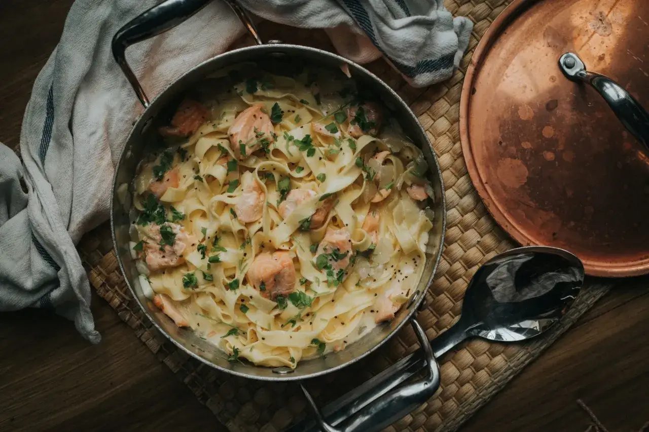 Tagliatelle al salmone in cremiger Sauce, garniert mit frischer Petersilie und schwarzem Pfeffer. Ein köstliches Gericht, das zum Genießen einlädt.