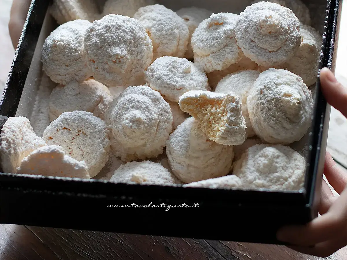 Deliziosi biscotti al cocco, soffici e ricoperti di zucchero a velo, in una scatola nera.