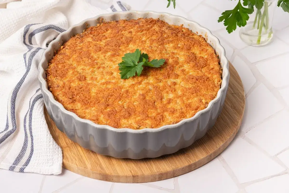 Pastel de bacalao dorado y crujiente, reci&eacute;n horneado en un molde gris, decorado con perejil fresco.