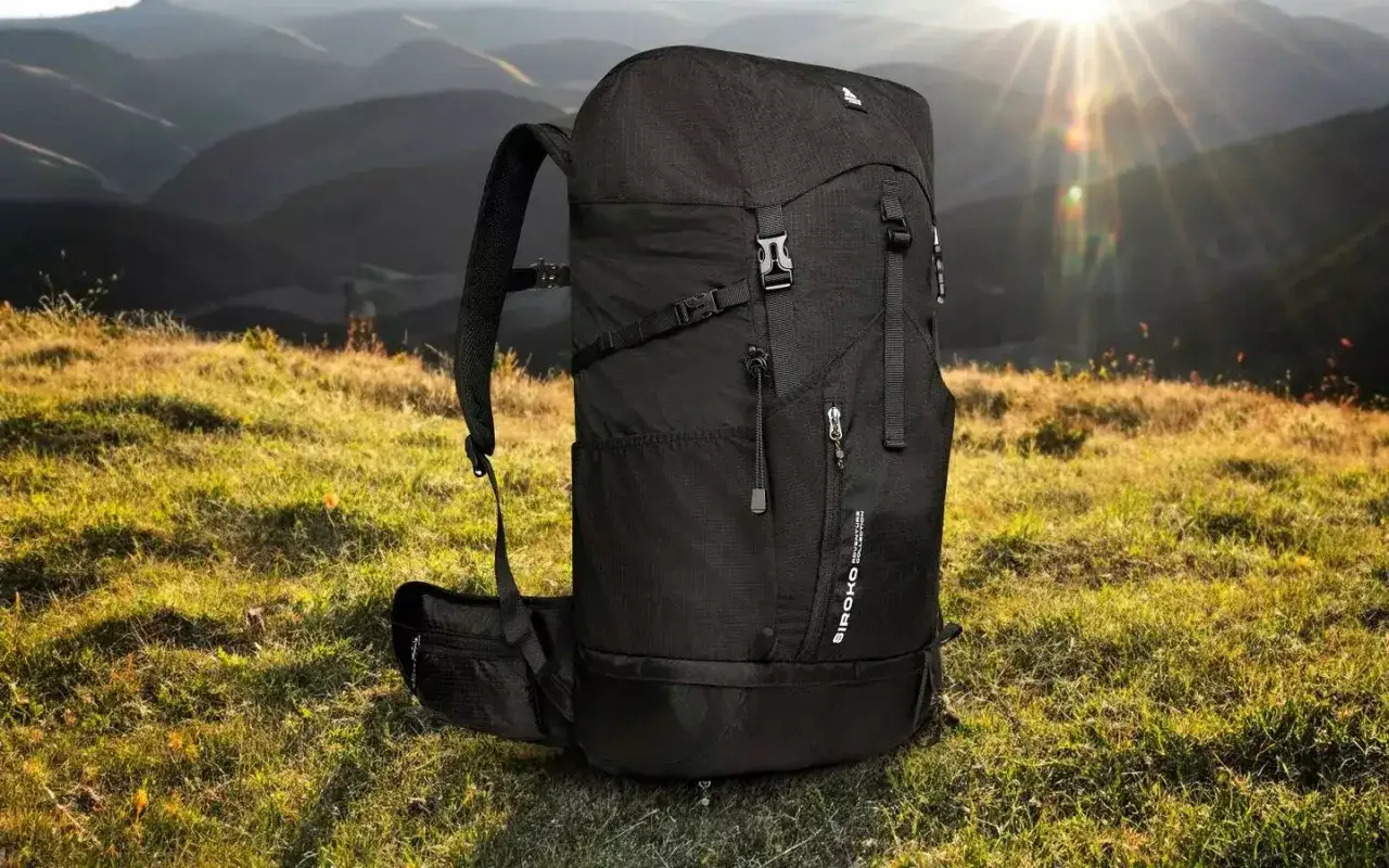 Czarny plecak gotowy na hiking i trekking, z pasem biodrowym, na tle górskiego krajobrazu o zachodzie słońca.