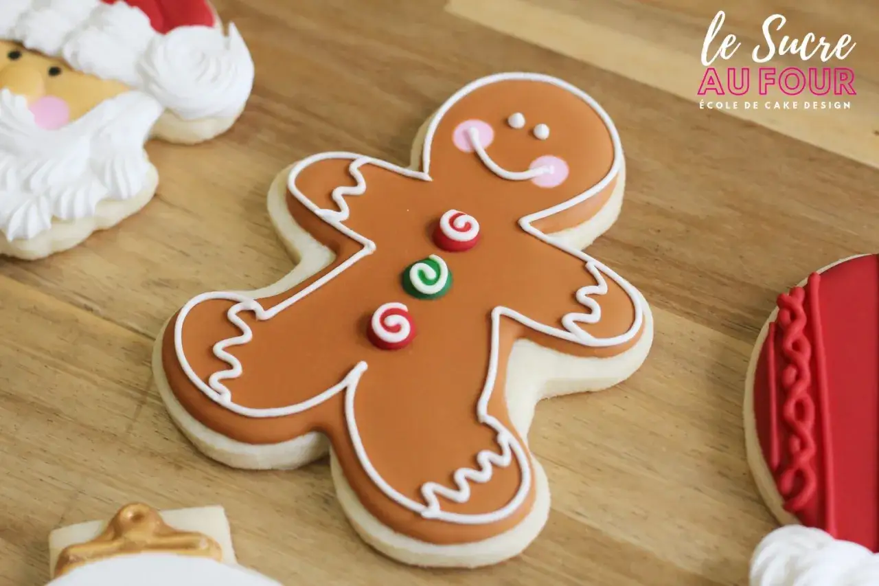 Un biscuit bonhomme pain d'épice souriant, décoré de glacage royal, avec des touches de rouge et vert.
