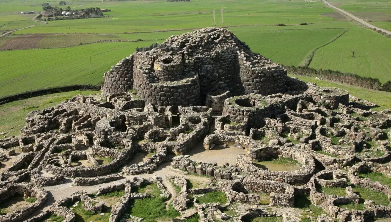 Resti di un complesso nuragico, con torri circolari e un villaggio circostante, immersi in un paesaggio rurale verdeggiante. Testimonianza della civilt&agrave; nuragica.